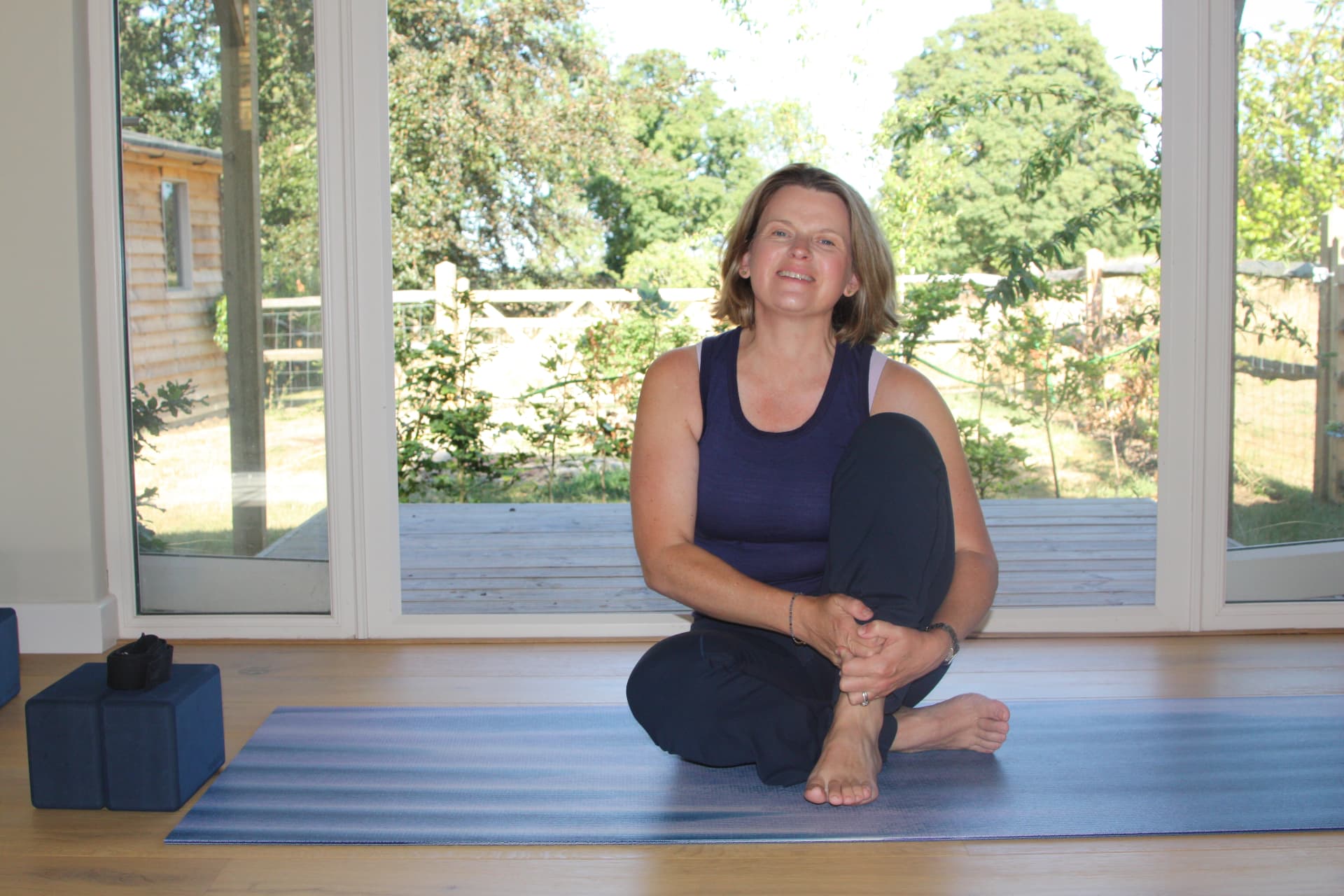 Floss Keville sitting cross-legged on a yoga mat in front of open studio doors